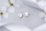 Load image into Gallery viewer, Silver flower-shaped earrings on a light gray background with white flowers.
